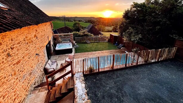 A stone house with a hot tub, a wooden deck, and a view of the sunset over a green landscape. - La Grange aux Souvenirs - Perigord Noir (Les Coteaux Périgourdins)