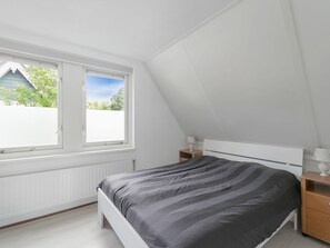 A bedroom with a bed, two bedside tables, a window, and a radiator. - Holiday Home With Enclosed Garden (Zonnemaire)
