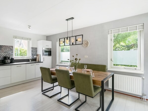 A modern kitchen with white cabinets, a wooden dining table, and green chairs. - Holiday Home With Enclosed Garden (Zonnemaire)