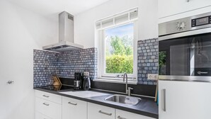 Una cocina moderna con armarios blancos, encimera negra, pileta de acero inoxidable y horno empotrado.