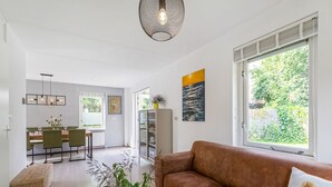 Una sala de estar moderna con un sofá de cuero marrón, un comedor con mesa y sillas de madera, y un ventanal con vistas a zonas verdes.