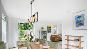 Un comedor con una mesa de madera dispuesta para cuatro personas, un sofá verde, una estantería de madera y vistas al exterior.