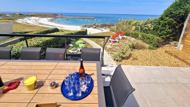 En terrasse med et bord dækket til drinks, med udsigt over en strand med både og parasoller.
