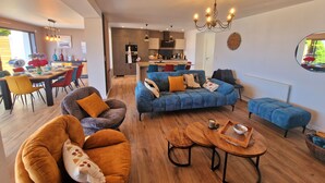 En moderne stue med sofa, lænestole og et spiseområde med bord og stole.