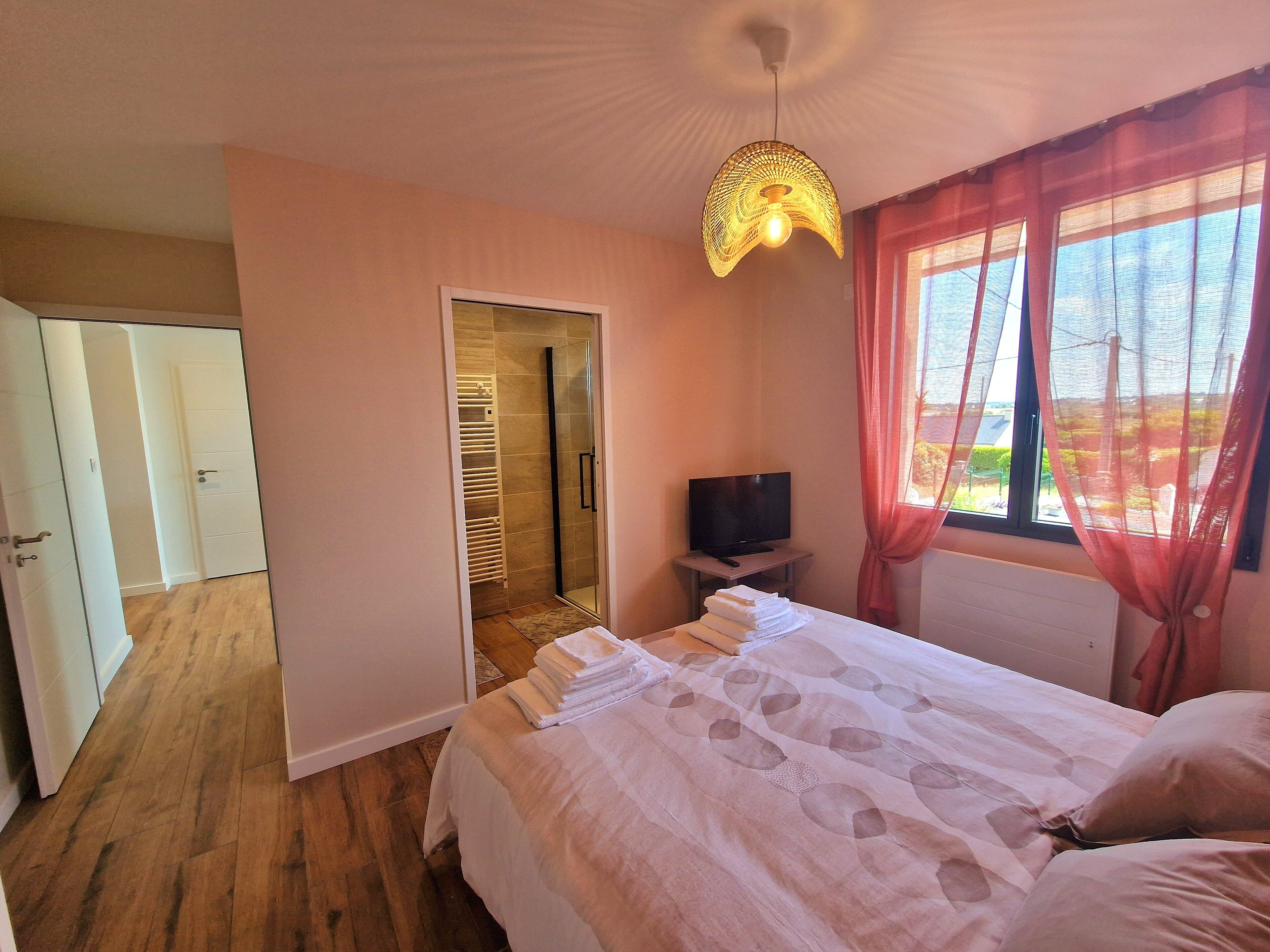 Una habitación de hotel con cama, televisor, cabina de ducha de vidrio y puerta que da a un pasillo.