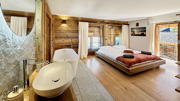 Une chambre moderne avec un plancher en bois, un grand lit, une baignoire intégrée et un grand miroir.