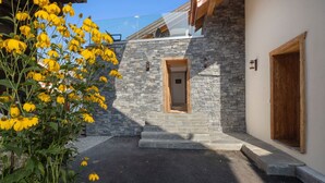 Un bâtiment moderne avec une façade en pierre, une porte en bois et des marches menant à l’entrée.