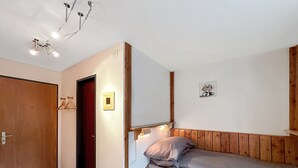 A bedroom with a wooden headboard, a bed with grey bedding, a wooden door, and a wall-mounted light fixture. - Haus Cresta - Zermatt Paradise- Swiss Alps (Zermatt)