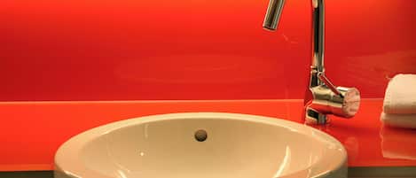 Un lavamanos blanco con grifo cromado en un baño con pared roja.