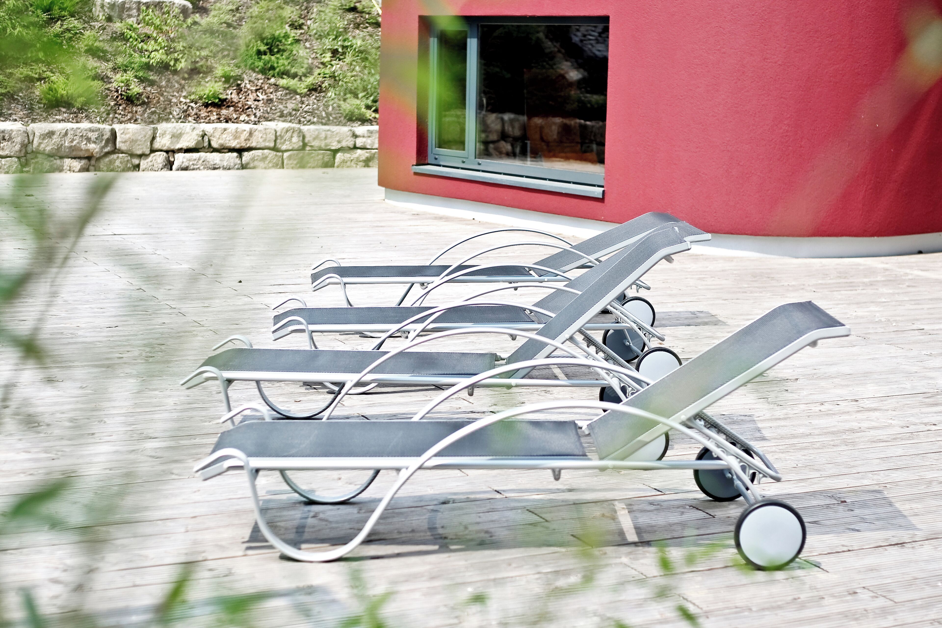 A row of sun loungers on a wooden deck with a red building in the background.