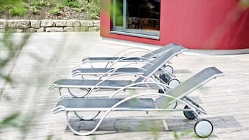 A row of sun loungers on a wooden deck with a red building in the background.