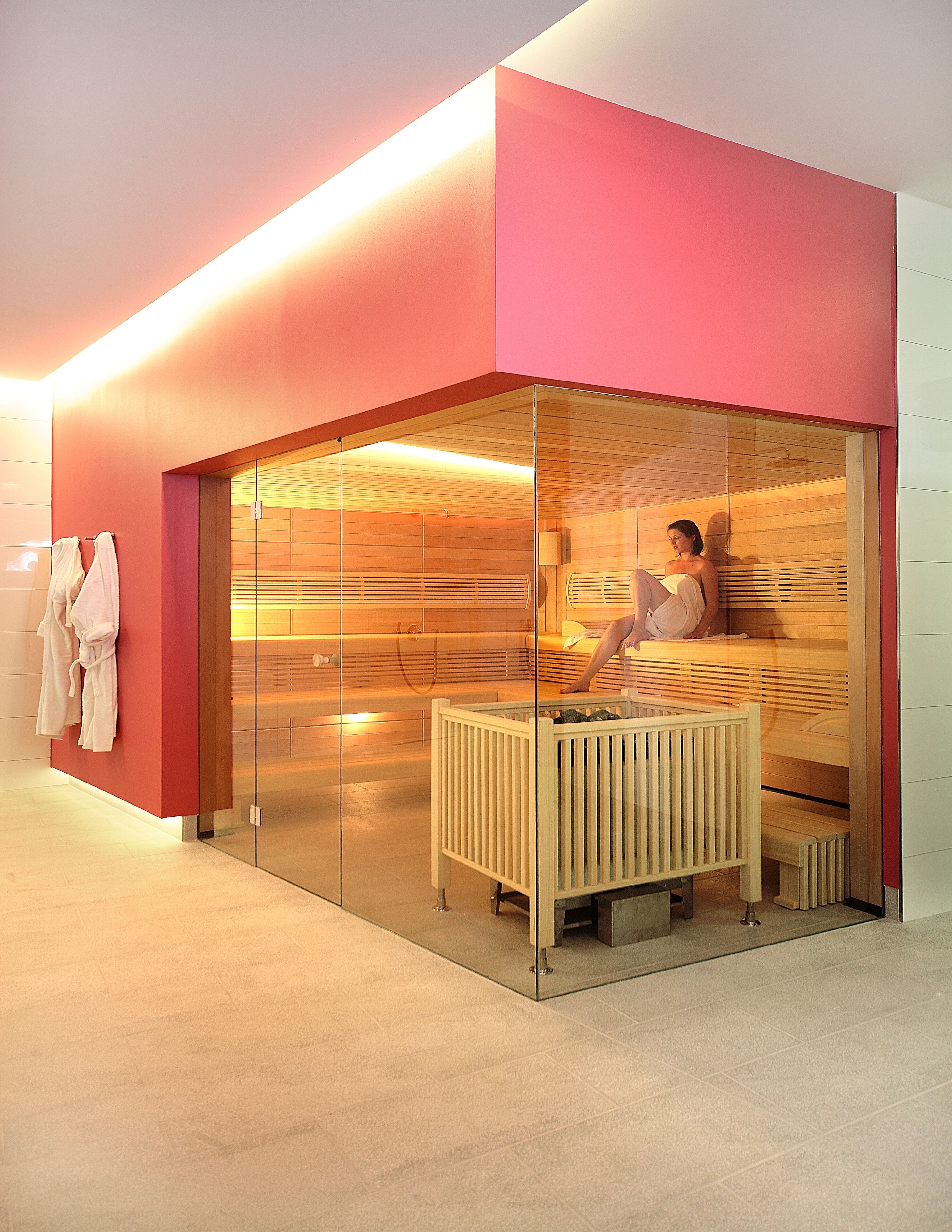 Une salle de spa moderne dotée d’une paroi en verre, de bancs en bois et d’un porte-serviettes avec des peignoirs.