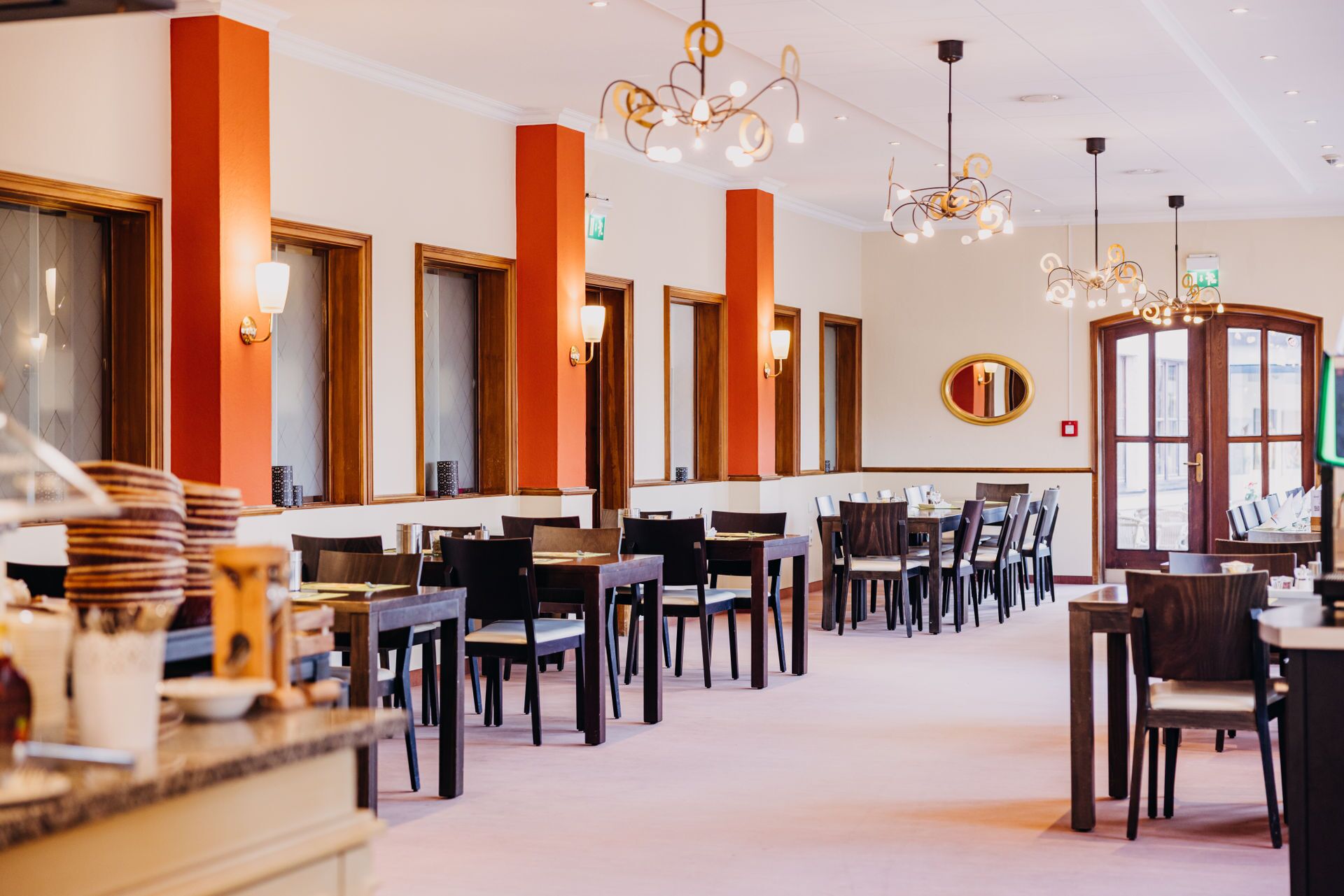 Ein Restaurant mit mehreren Tischen und Stühlen, einer Kristallleuchter und einem großen Spiegel an der Wand.