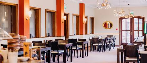 Un restaurante con varias mesas y sillas, un candelabro y un espejo grande en la pared.