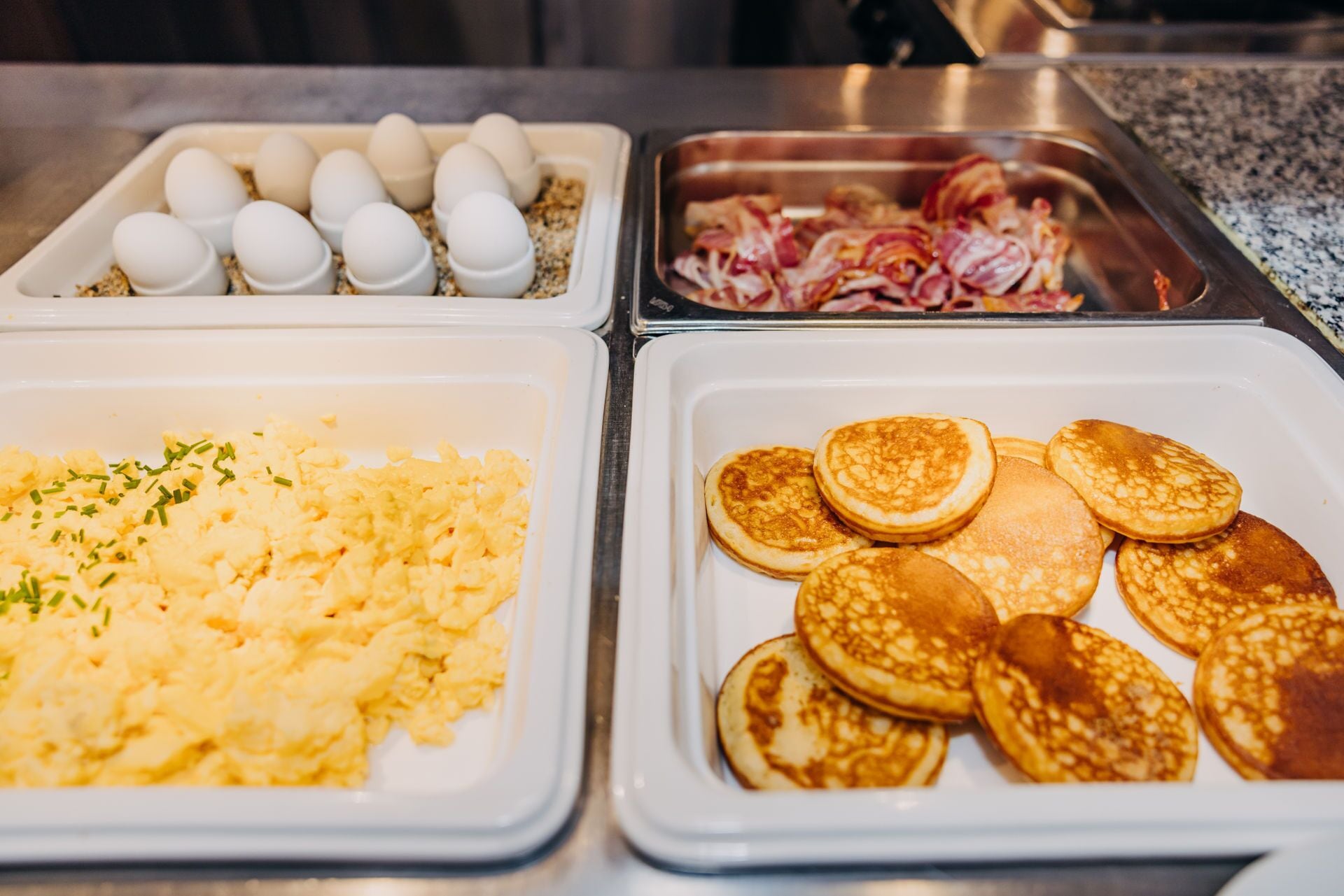 Un buffet de petit-déjeuner avec des œufs brouillés, du bacon et des crêpes.