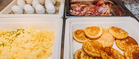 Un buffet de petit-déjeuner avec des œufs brouillés, du bacon et des crêpes.