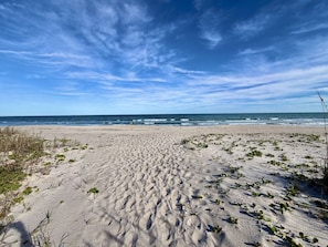 A sandy beach with sparse vegetation and a clear sky.