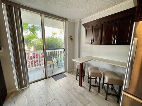 A kitchen with a sliding glass door leading to a balcony, a refrigerator, and a small dining area with stools.