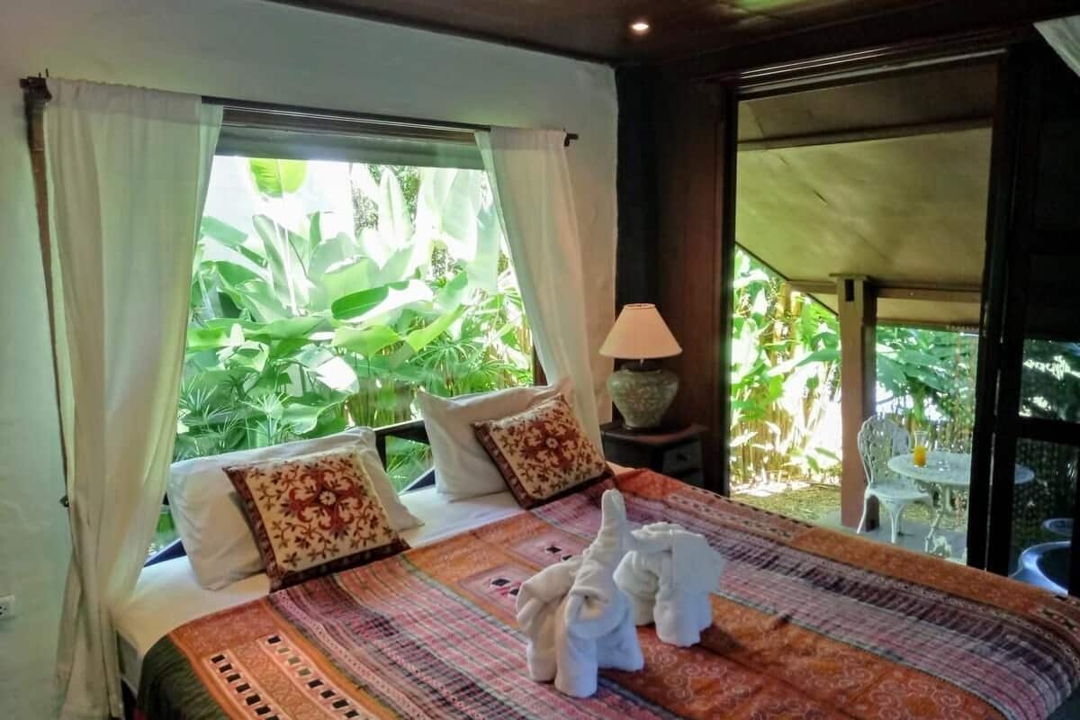 Un dormitorio con una cama grande, cortinas blancas y vistas a un follaje exuberante.