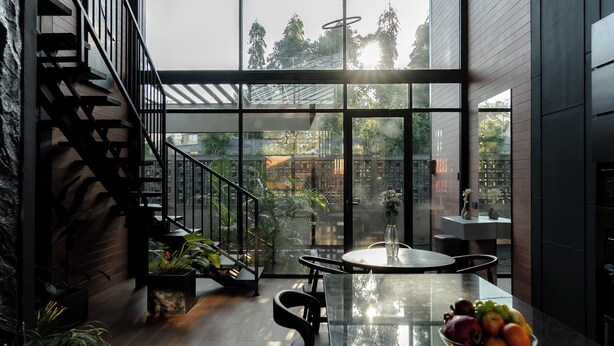 Een modern interieur met een glazen wand, een trap en een eethoek met een fruitschaal.