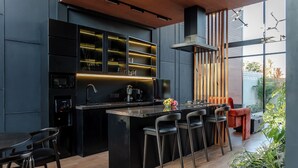 Een moderne keuken met een centraal eiland, barkrukken en een zithoek met een rode stoel.