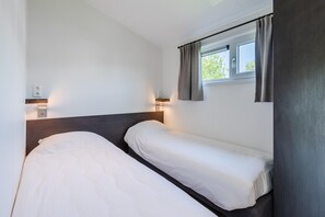 A single bed with a wooden headboard and a window with curtains.