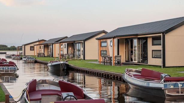 Uma fileira de casas modernas, térreas, com grandes janelas e um canal em frente.
