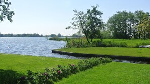 A serene lakeside park with a grassy area, a small dock, and trees. - Chalet With Private Jetty (Giethoorn)