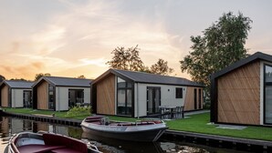 Uma fileira de casas modernas térreas, com grandes janelas, gramado e um canal com um barco atracado na frente.