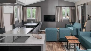 Uma cozinha moderna com uma ilha central, área de jantar com mesa e cadeiras, espaço de estar com sofás e uma TV fixada na parede.
