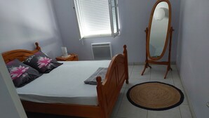 Un dormitorio con una cama de madera, una mesita de noche con lámpara, un espejo y una ventana con persianas.