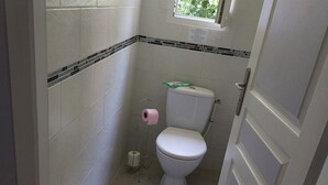 Un baño pequeño y limpio con azulejos blancos, un inodoro y una ventana.