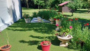 Un jardín cuidado con diversas plantas y flores en macetas, un cobertizo pequeño y un césped.
