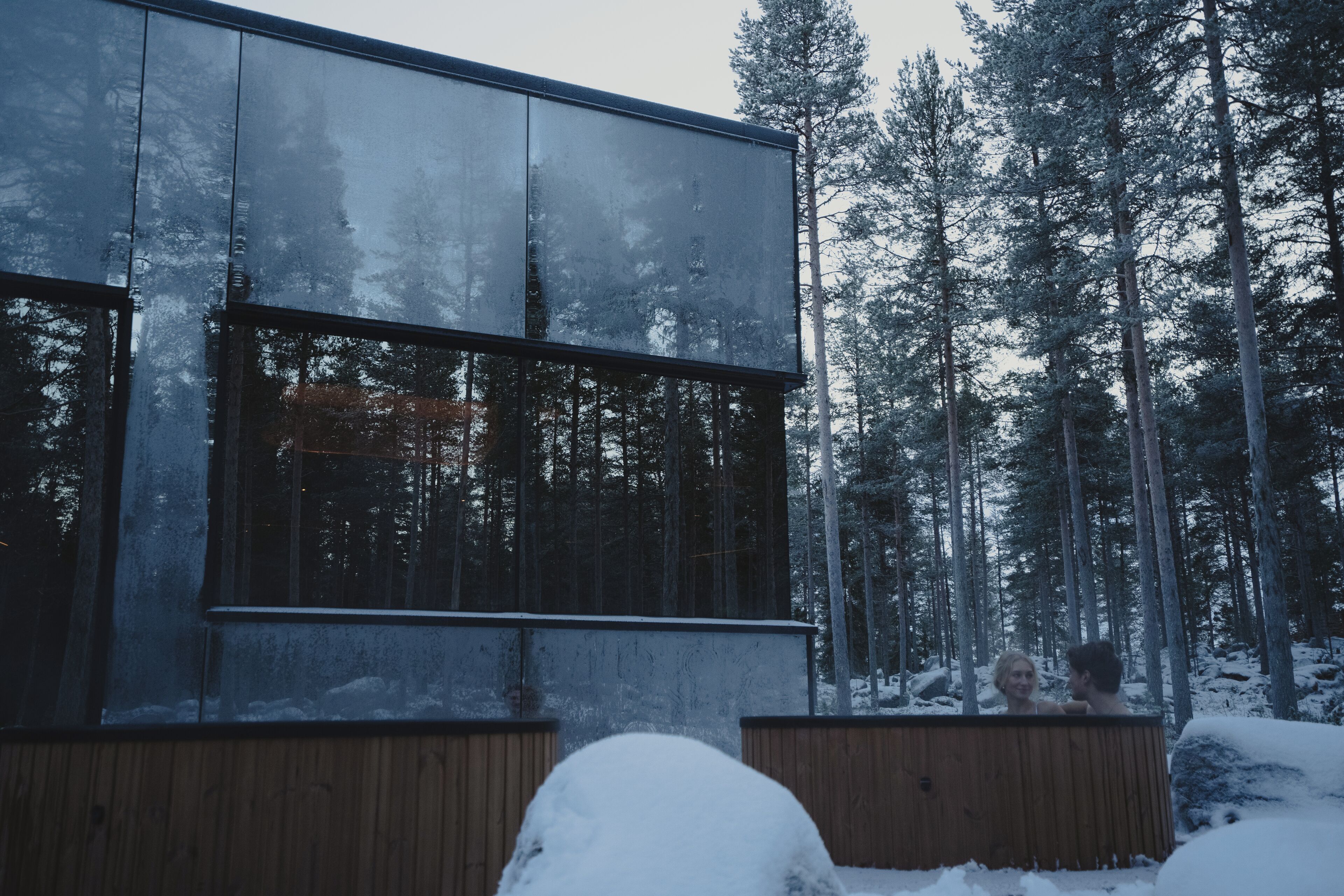 A modern building with large windows, surrounded by a snowy forest.