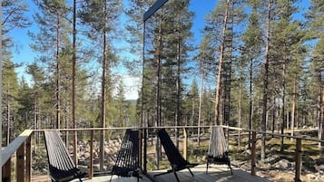 Puinen terassi, jossa on kaksi mustaa riippukeinua ja tuoli, ja sen ympärillä kohoaa korkeita mäntyjä.
