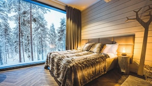 Un dormitorio con un gran ventanal, una cama con un edredón de aspecto aterciopelado, una mesita de noche con una lámpara y un panel de pared de madera.