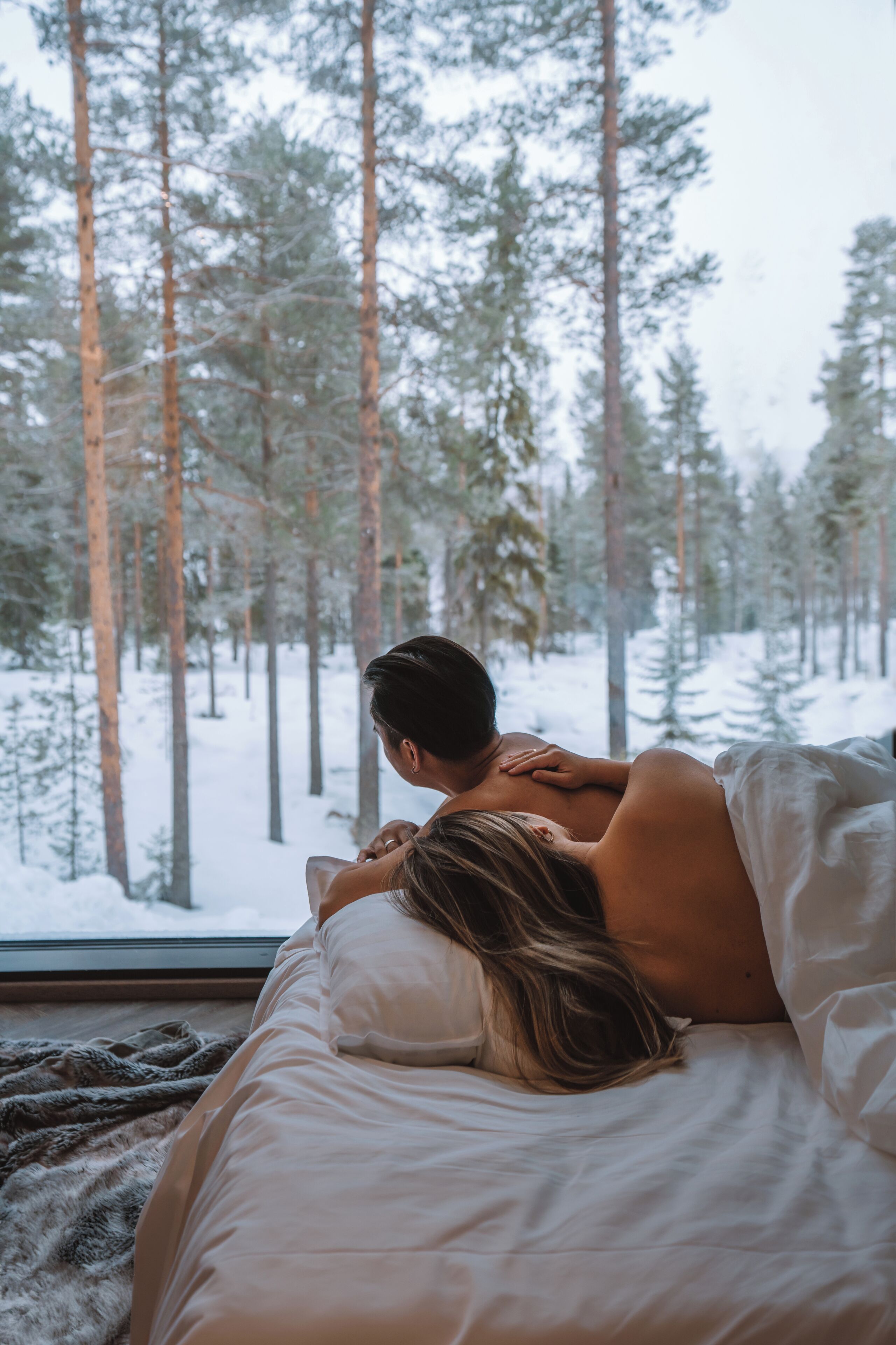 Ein Schlafzimmer mit einem Bett, einem Fenster und Blick auf einen verschneiten Wald.