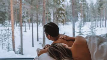 Ein Schlafzimmer mit einem Bett, einem Fenster und Blick auf einen verschneiten Wald.