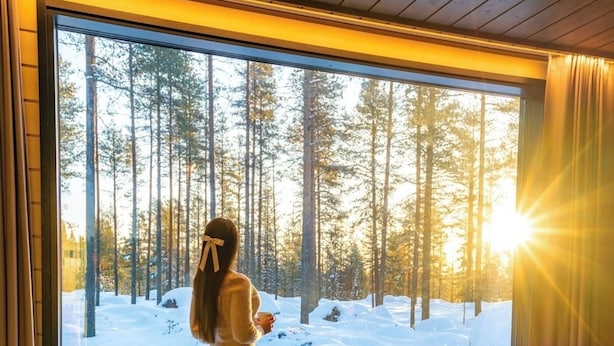 Una habitación con un ventanal grande que da a un bosque nevado, un sillón acogedor y una cama con una manta de piel.