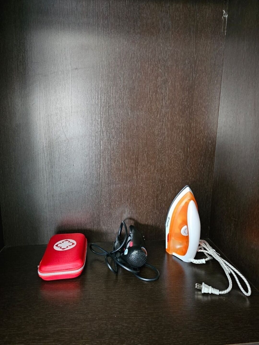 A wooden surface with a red bag, a black microphone, and an orange and white iron.