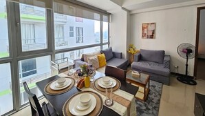 A modern living room with a dining table set for four, a grey sofa, and a standing fan. - Sunshine 100 Plaza (Mandaluyong)