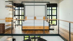 A modern bedroom with a large bed, wooden flooring, and a view of greenery through large windows. - Berawa Loft 10 by Betterplace (Canggu)
