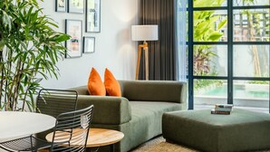 A modern living room with a green sofa, orange cushions, a round table with chairs, a floor lamp, and framed pictures on the wall. - Berawa Loft 10 by Betterplace (Canggu)
