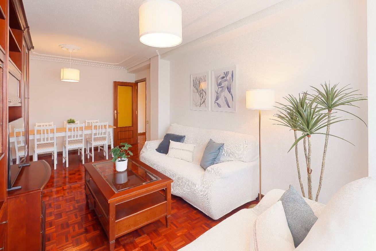 Una sala de estar con un sofá blanco, una mesa de centro de madera y un comedor con sillas blancas.
