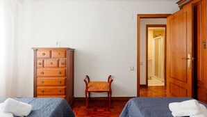 A room with two beds, a wooden dresser, a chair, and a door leading to another room. - 1A130 Coqueto apartamento cerca playa (Gijón)