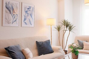 A living room with a beige sofa, two pillows, a floor lamp, and two potted plants.