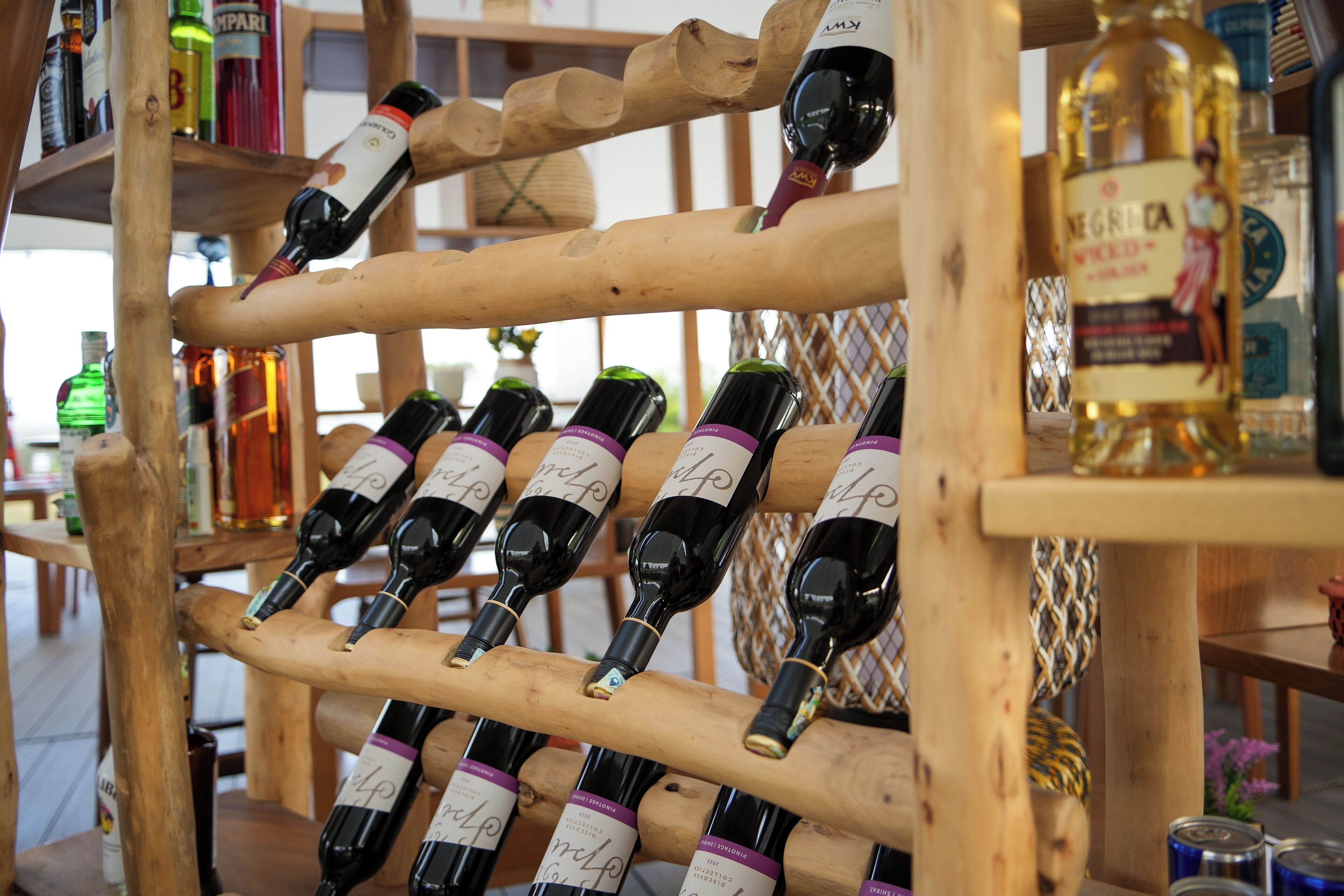 A wooden wine rack holding several bottles of wine, with a variety of other bottles and containers in the background.