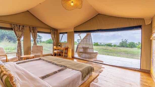 A tented room with a large bed, a desk, chairs, and a hanging chair. - Malaika Mara River Luxury Camp (Serengeti)