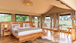 A spacious tent-style bedroom with a large bed, wooden headboard, and a view of the outdoors. - Malaika Mara River Luxury Camp (Serengeti)
