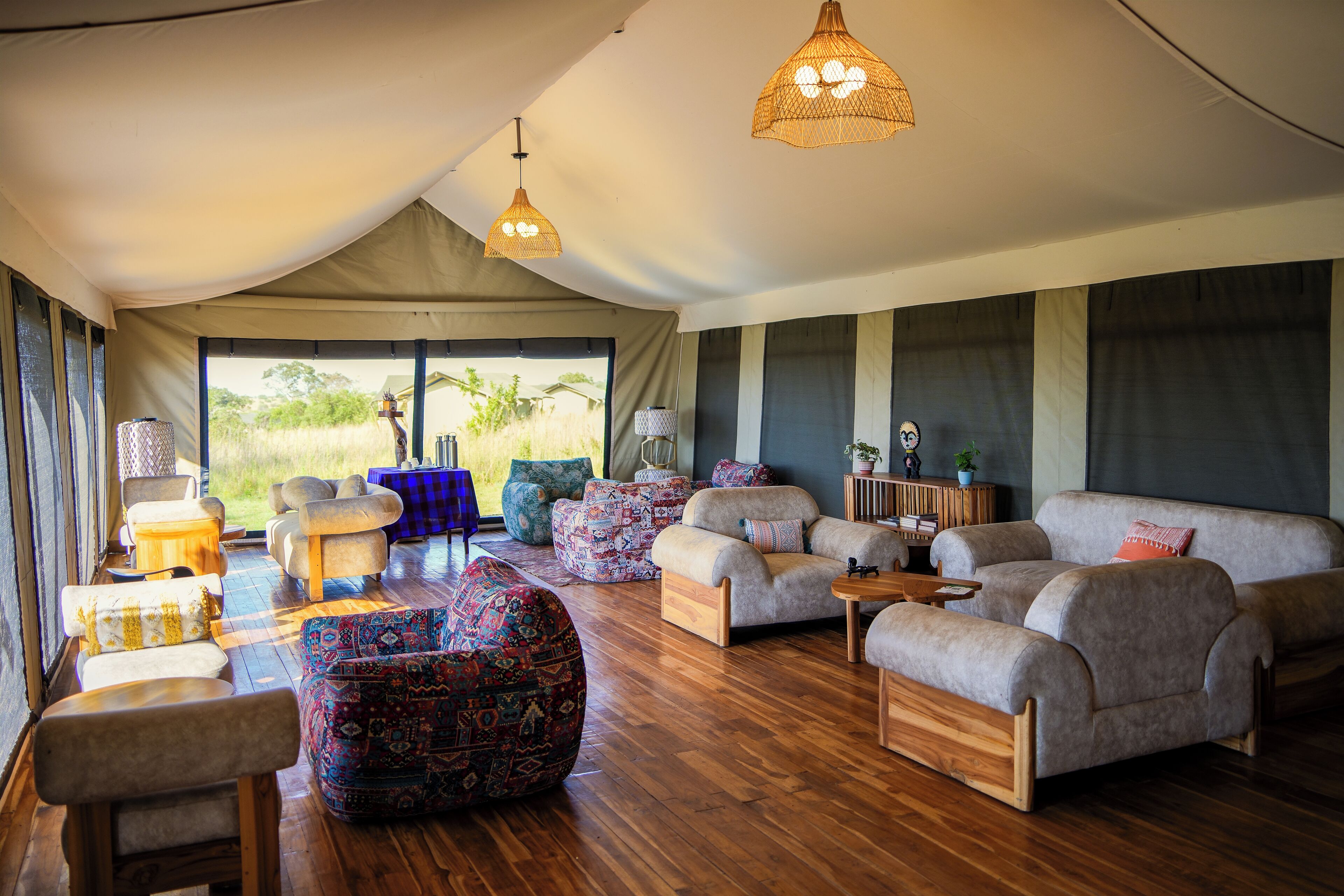 A spacious tented room with a wooden floor, multiple seating areas including sofas and chairs, and hanging woven light fixtures.